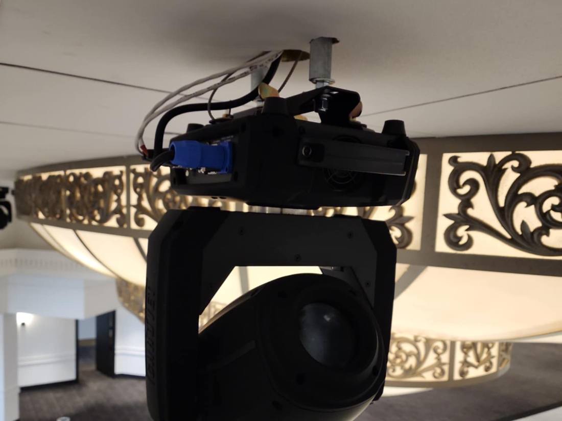 Moving-head lighting fixture mounted beside an ornate chandelier ring