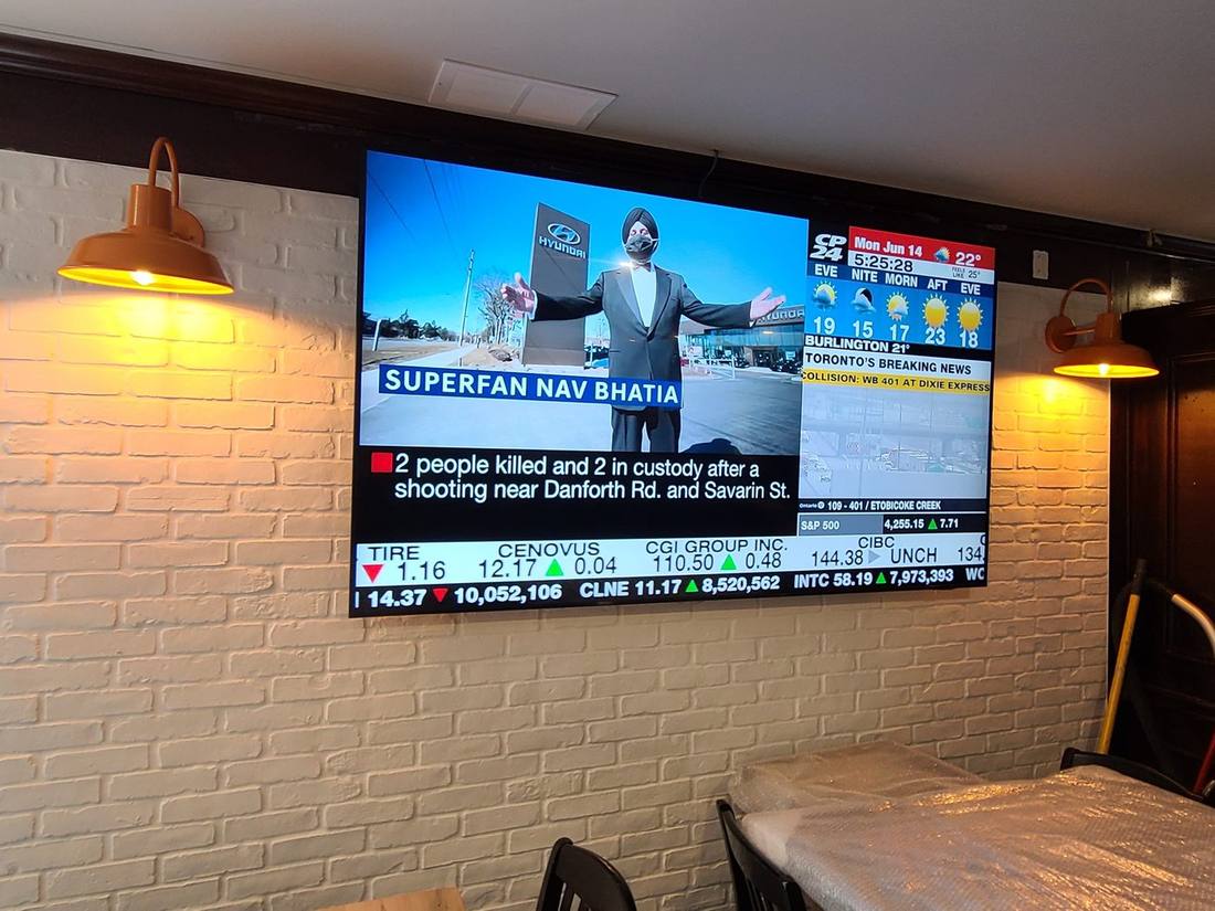 Large wall-mounted display on exposed brick showing a news broadcast