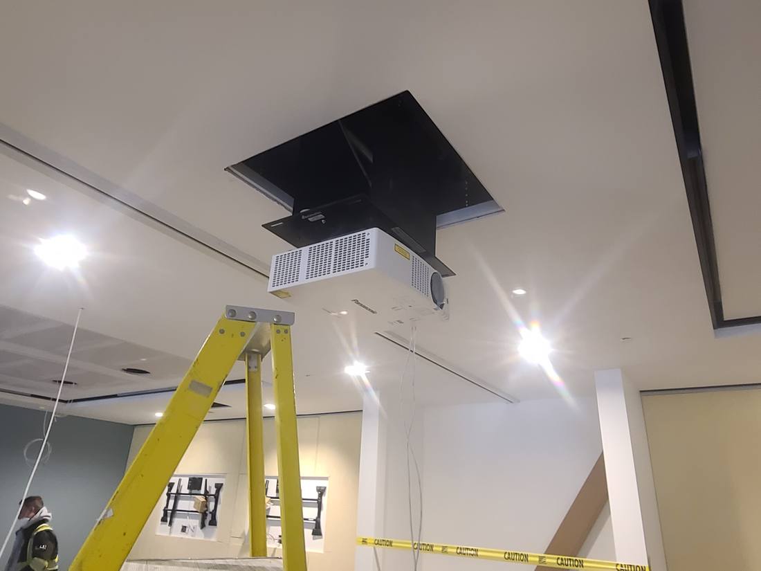 Technician installing a recessed ceiling projector from a ladder