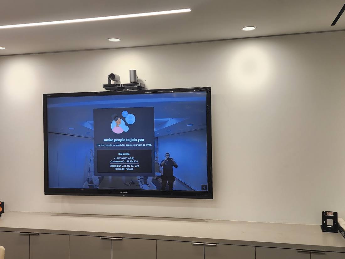Wall-mounted display showing a video conferencing invite screen in a boardroom